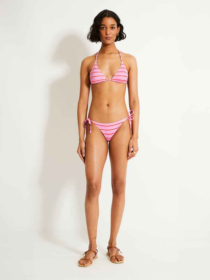 Woman Standing Wearing lemlem MALIA Triangle Top featuring soft pink color accented by neon orange red stripes and matching string bottom