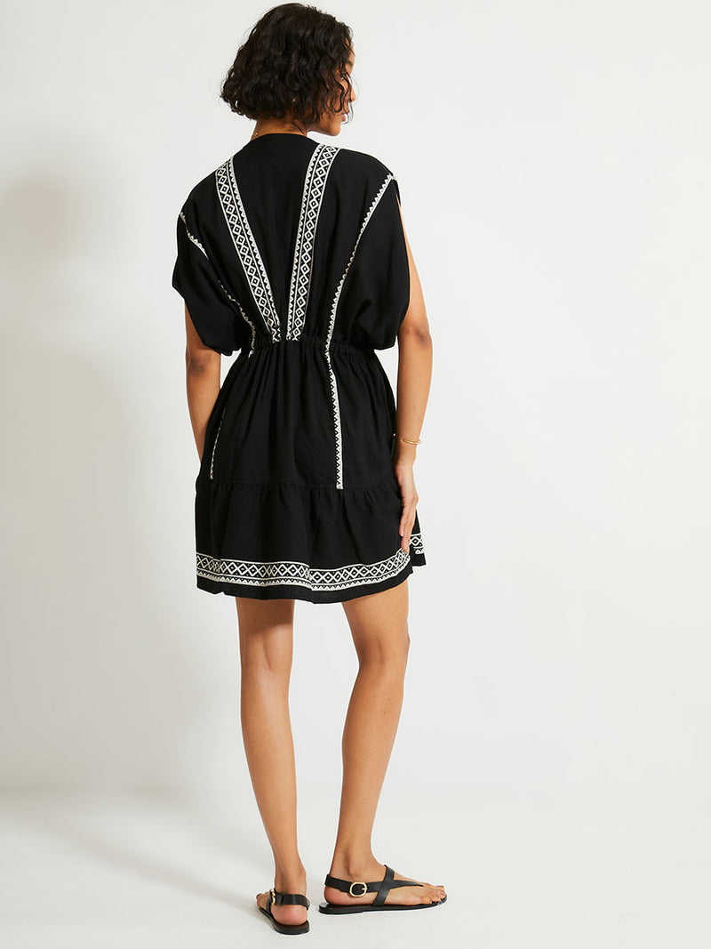 Back of a Woman Standing Wearing lemlem ALEM Plunge Dress Featuring rich black background with intricate cream Tibeb border pattern