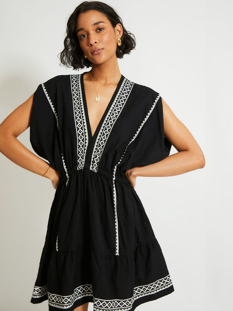 Woman Standing Wearing lemlem ALEM Plunge Dress Featuring rich black background with intricate cream Tibeb border pattern