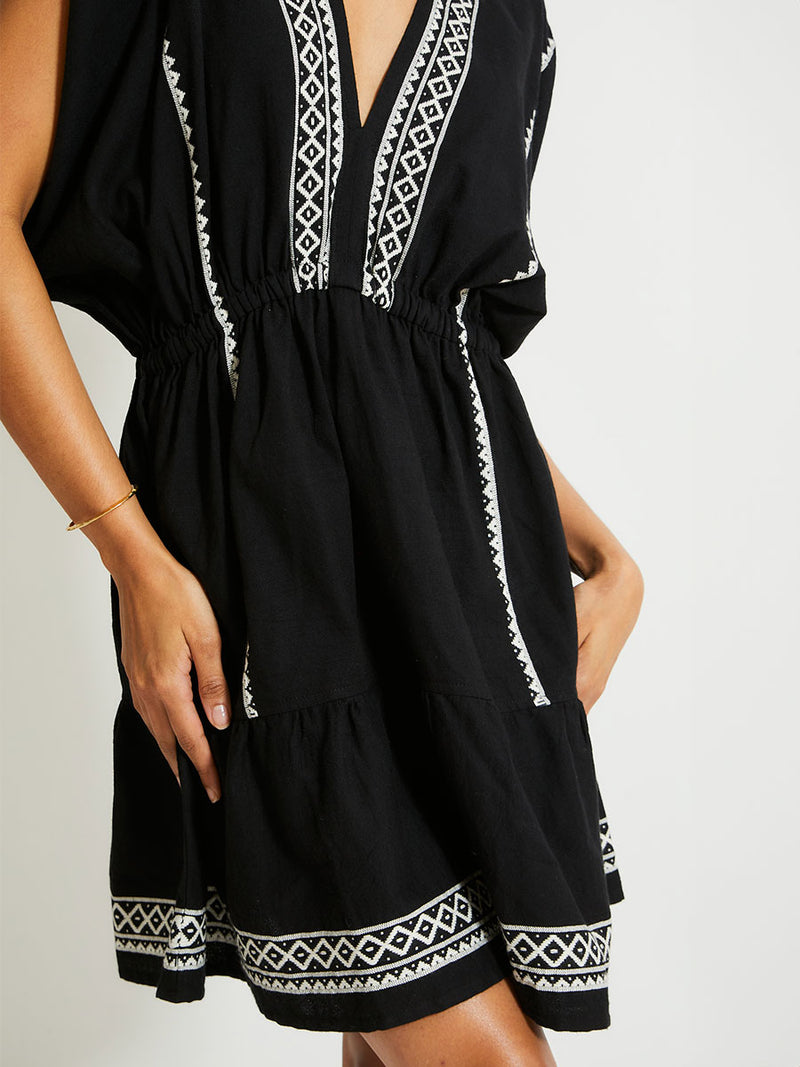 Close up on a Woman Standing Wearing lemlem ALEM Plunge Dress Featuring rich black background with intricate cream Tibeb border pattern