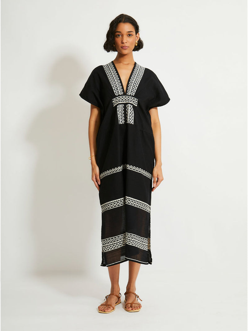 Woman Standing Wearing lemlem GASIRA Caftan Featuring rich black background with intricate cream Tibeb border pattern