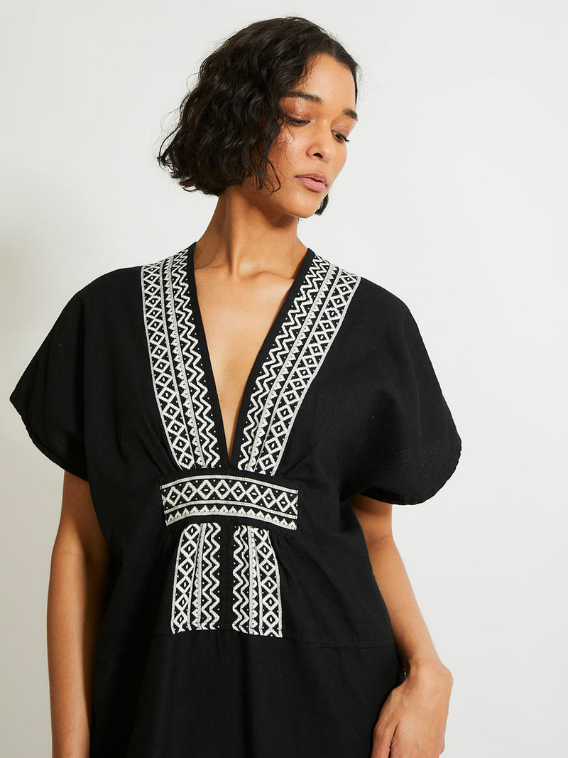 Close up on a Woman Standing Wearing lemlem GASIRA Caftan Featuring rich black background with intricate cream Tibeb border pattern