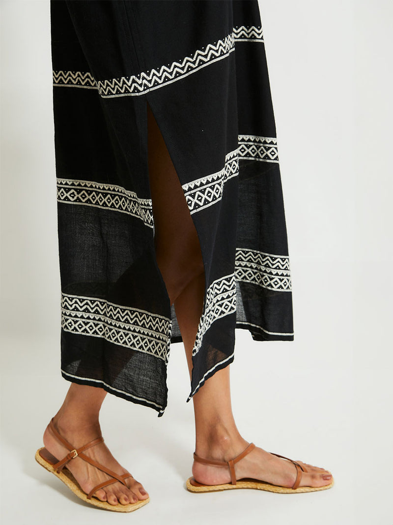 Close up on Woman's legs Standing Wearing lemlem GASIRA Caftan Featuring rich black background with intricate cream Tibeb border pattern