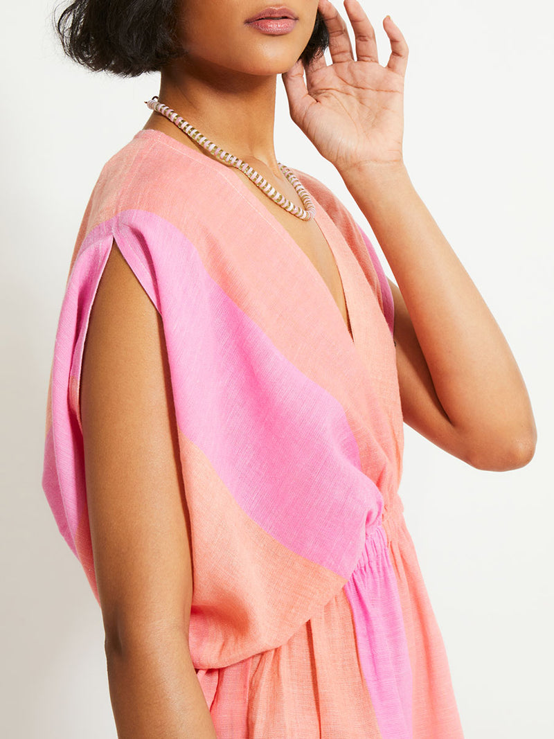 Close up on a Woman Standing Wearing lemlem ALEM Plunge Dress featuring light, gauzy fabric with a beautiful ombre color block of pink, blush, and peach colors.