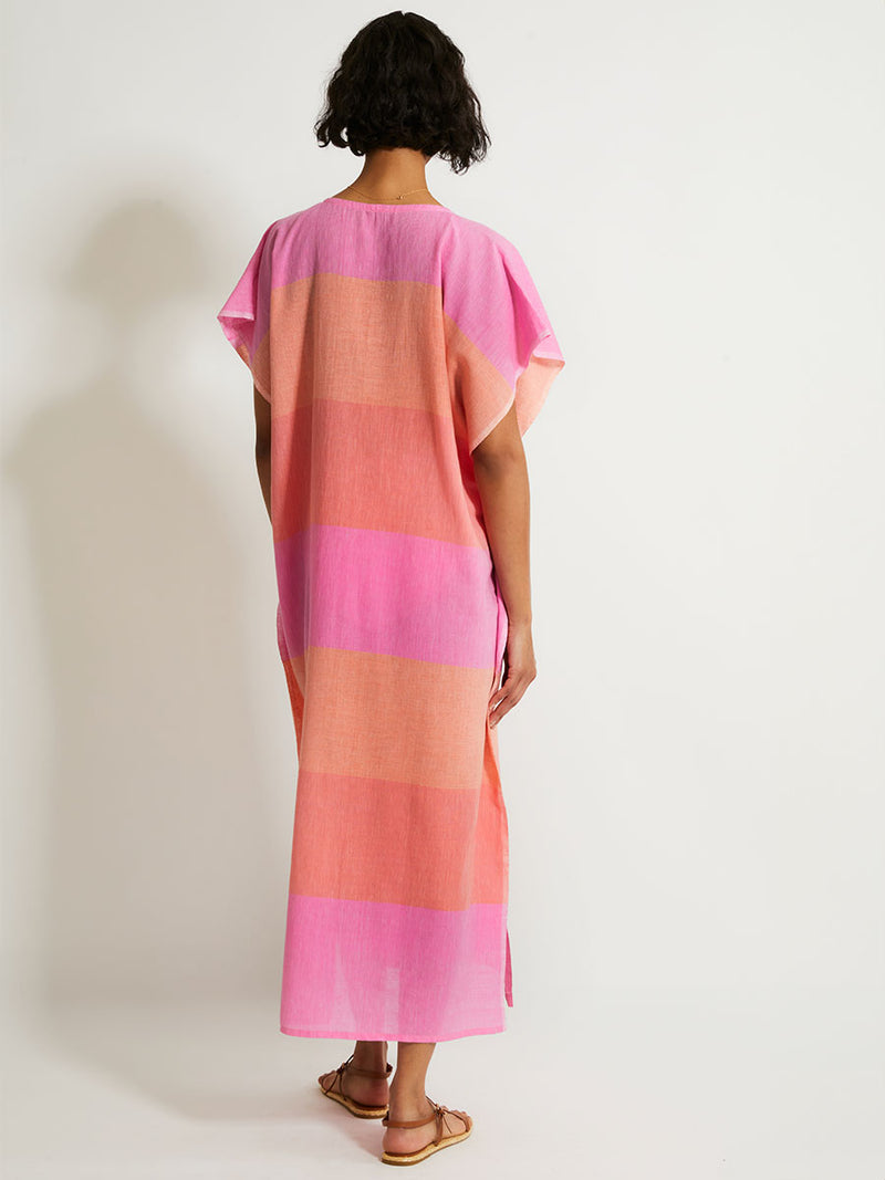 Back of a Woman Standing Wearing lemlem DALILA Caftan featuring gauzy fabric with a beautiful ombre color block of pink, blush, and peach colors.