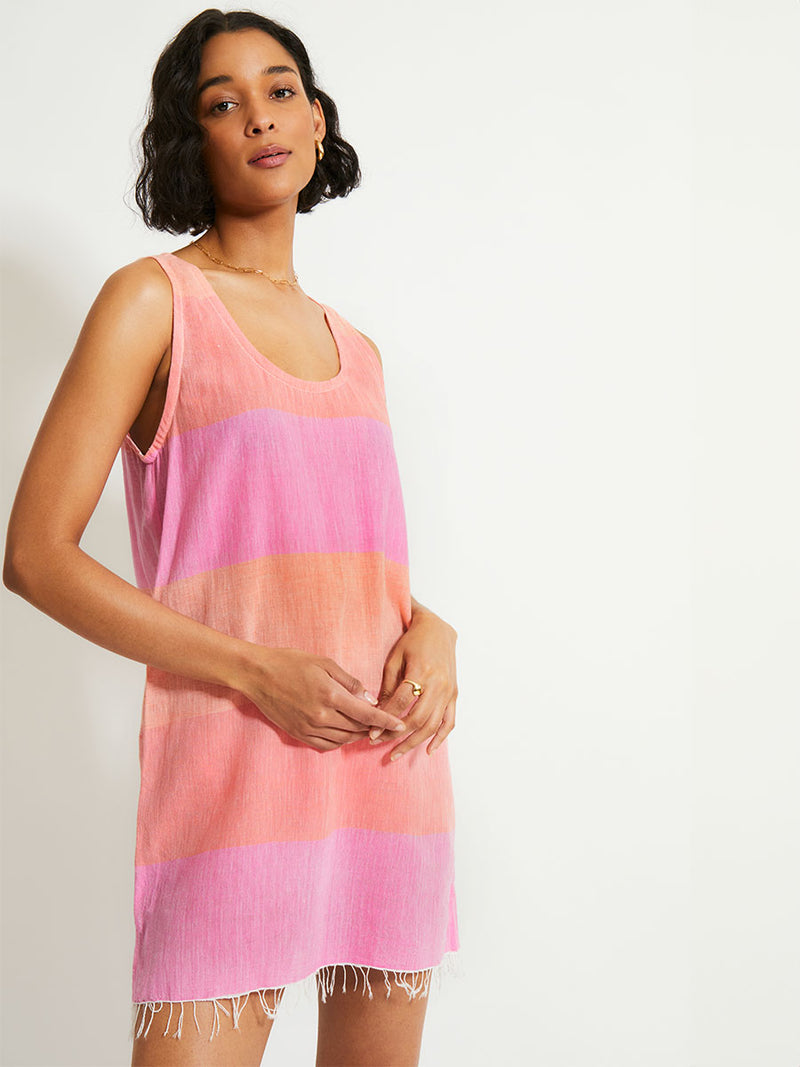 Woman Standing Wearing lemlem MAHLET Dress featuring gauzy fabric with a beautiful ombre color block of pink, blush, and peach colors.