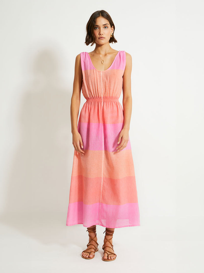 Woman Standing Wearing lemlem Melat Scoop Dress featuring gauzy fabric with a beautiful ombre color block of pink, blush, and peach colors.