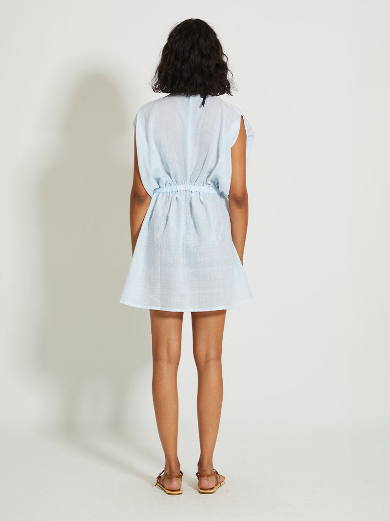 Back of a Woman Standing Wearing lemlem Alem Plunge Dress featuring airy gauze fabric in a delicate pale blue color.