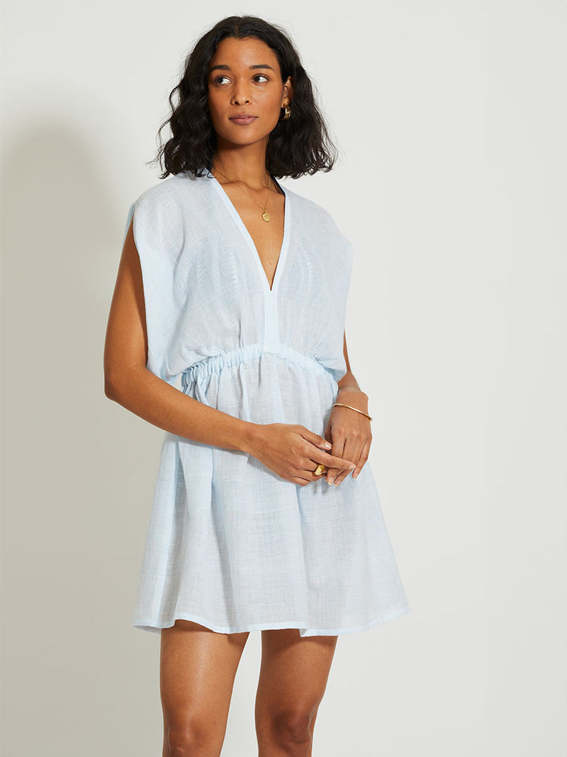 Woman Standing Wearing lemlem Alem Plunge Dress featuring airy gauze fabric in a delicate pale blue color.