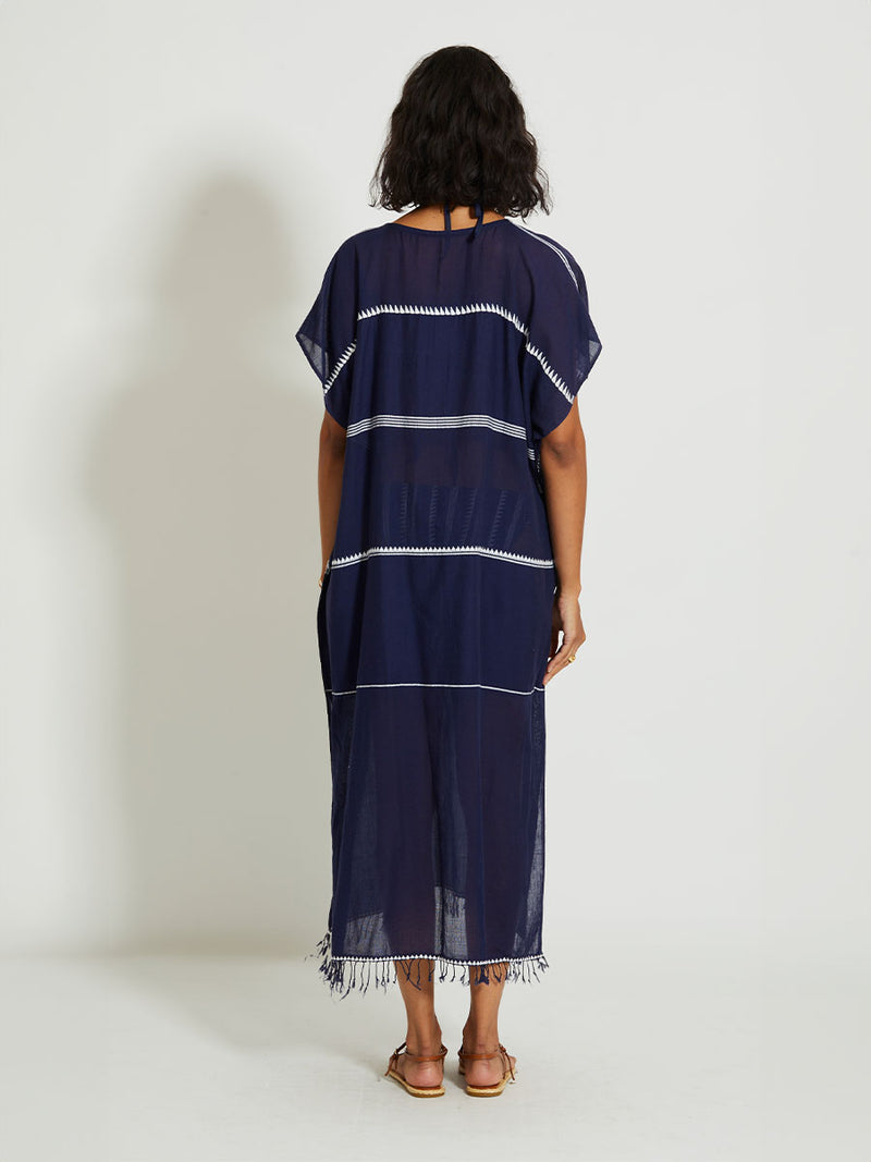 Back of a Woman standing wearing the Nunu classic caftan in navy blue featuring white stripes and graphic lines.