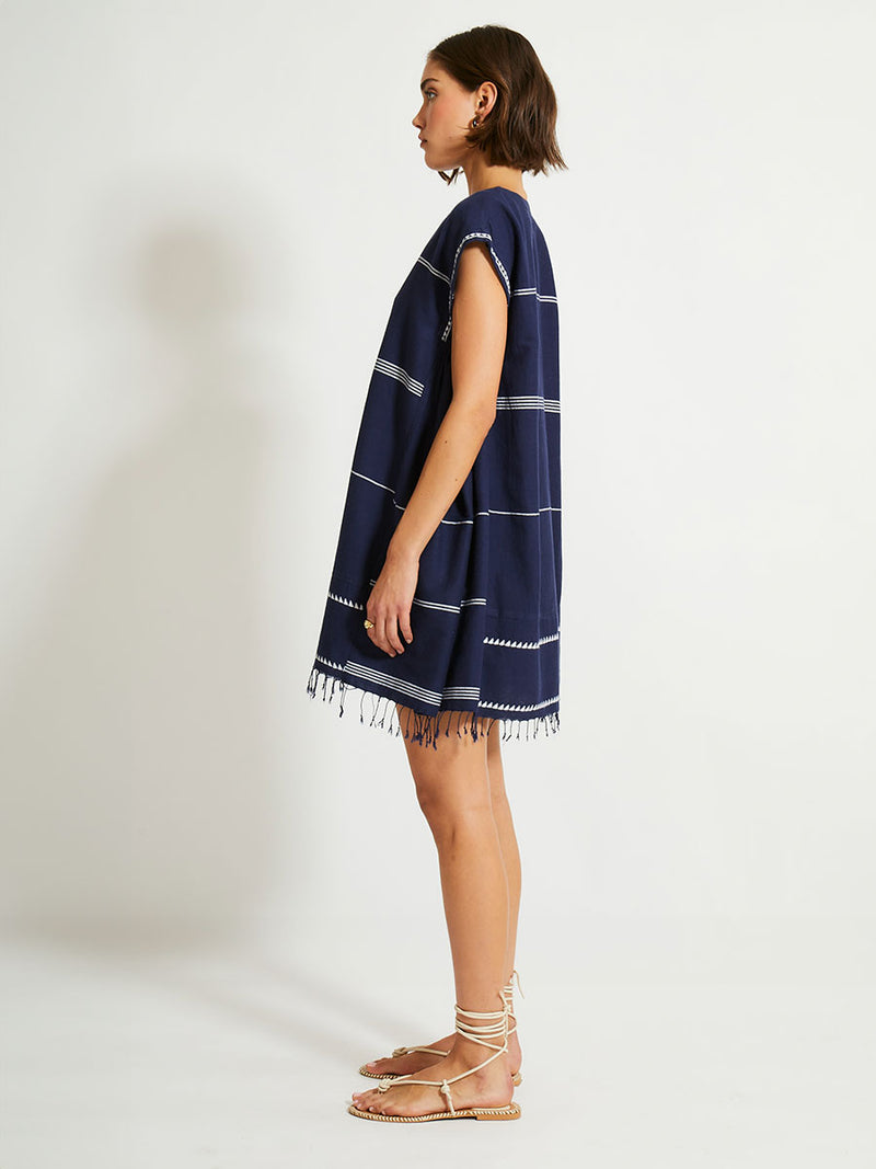 Side Shot of a Woman Standing Wearing lemlem ELINA Caftan featuring  delicate white Tibeb bands on a rich navy background