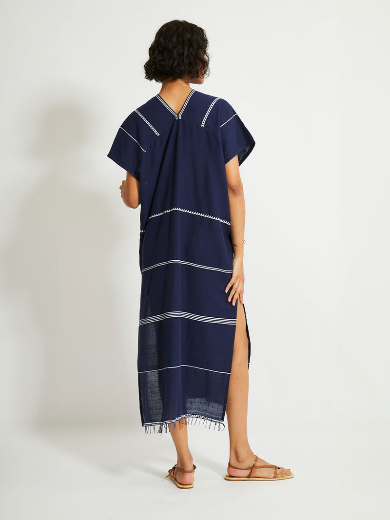 Back of a Woman Standing Wearing  lemlem GASIRA Caftan featuring delicate white Tibeb bands on a rich navy background