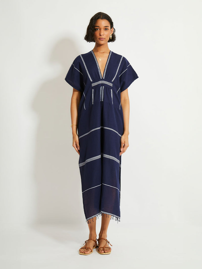 Woman Standing Wearing  lemlem GASIRA Caftan featuring delicate white Tibeb bands on a rich navy background