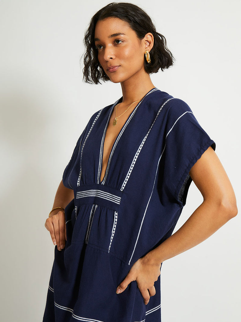 Close up on a Woman Standing Wearing  lemlem GASIRA Caftan featuring delicate white Tibeb bands on a rich navy background