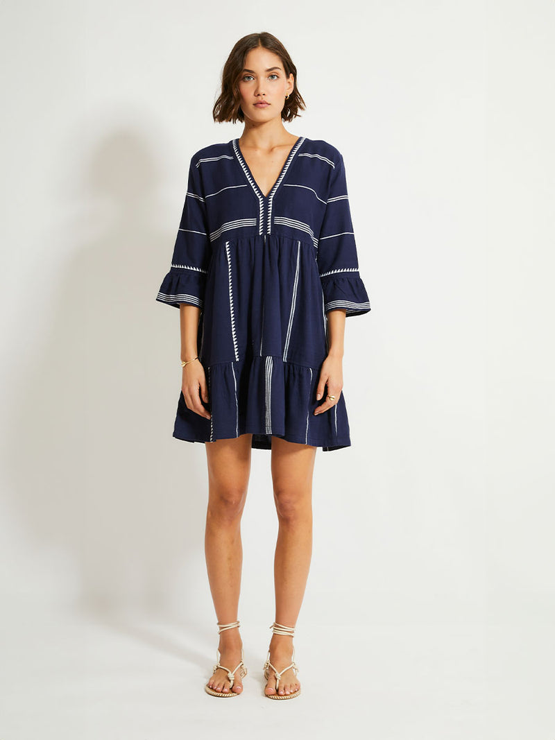 Woman Standing Wearing lemlem HANNA Flutter Dress in Nunu Navy featuring delicate white Tibeb bands on a rich navy background