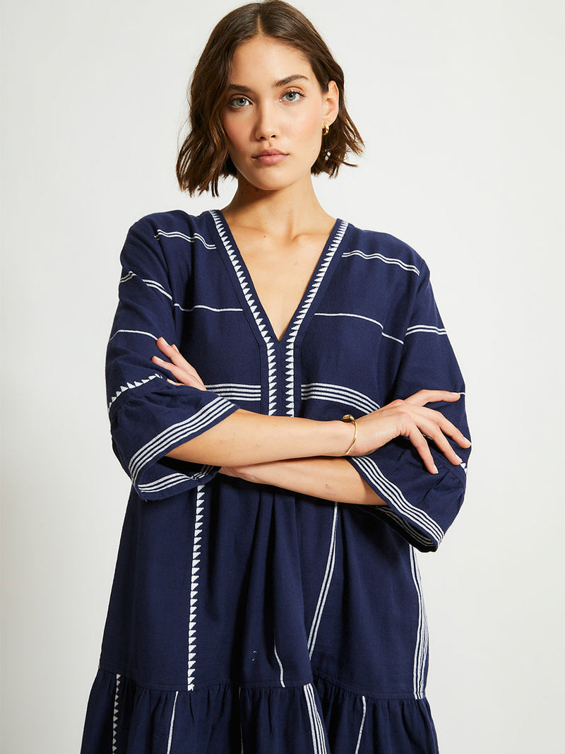 Woman Standing Wearing lemlem HANNA Flutter Dress in Nunu Navy featuring delicate white Tibeb bands on a rich navy background