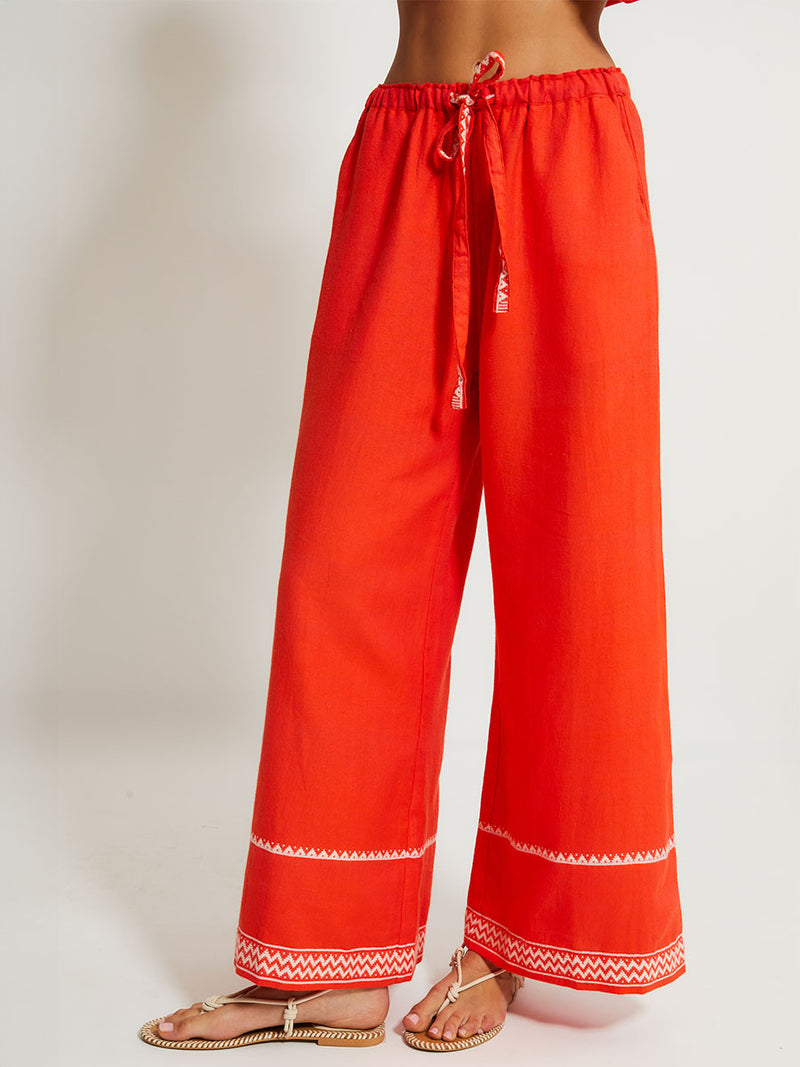 Close up on a Woman Standing Wearing lemlem DESTA Pants featruing an intricate Tibeb pattern in rich red and vanilla colors