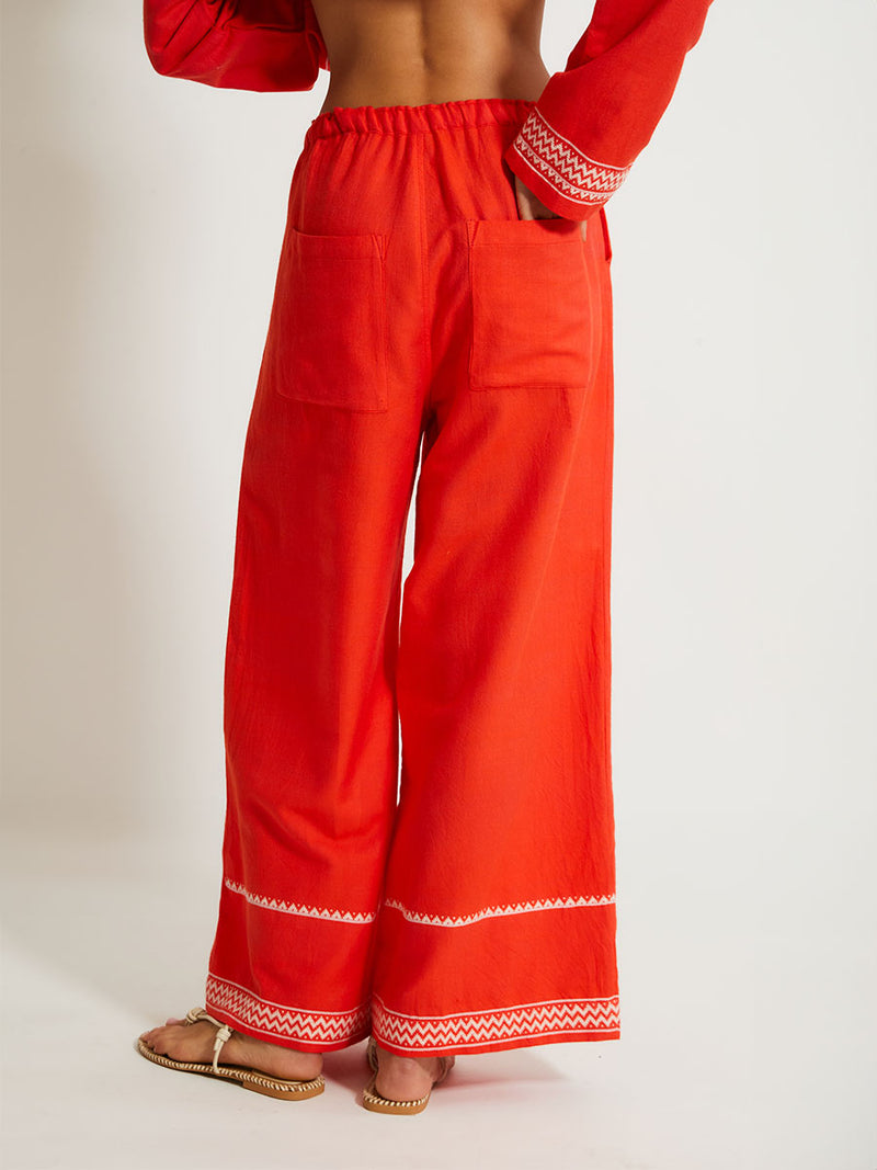 Close up on a back of a Woman Standing Wearing lemlem DESTA Pants featruing an intricate Tibeb pattern in rich red and vanilla colors