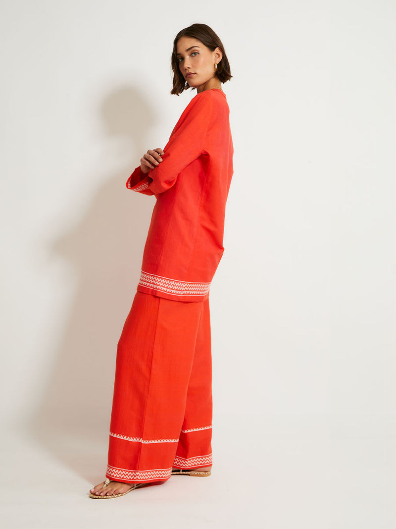 Side of a Woman Standing Wearing lemlem DESTA Pants featruing an intricate Tibeb pattern in rich red and vanilla colors