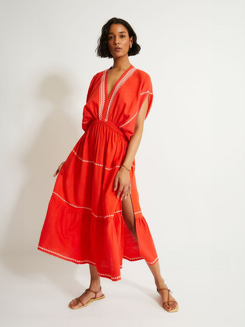 Woman Standing Wearing lemlem LELISA Dress featruing an intricate Tibeb pattern in rich red and vanilla colors