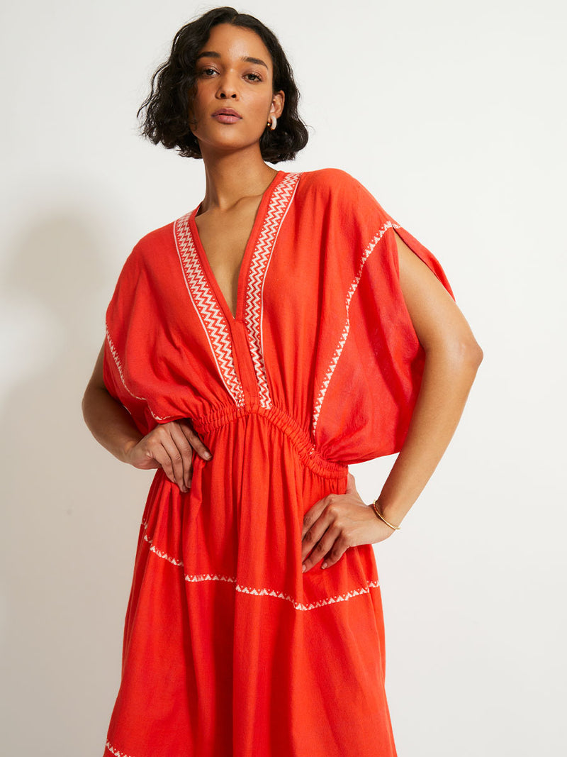 Woman Standing Wearing lemlem LELISA Dress featruing an intricate Tibeb pattern in rich red and vanilla colors