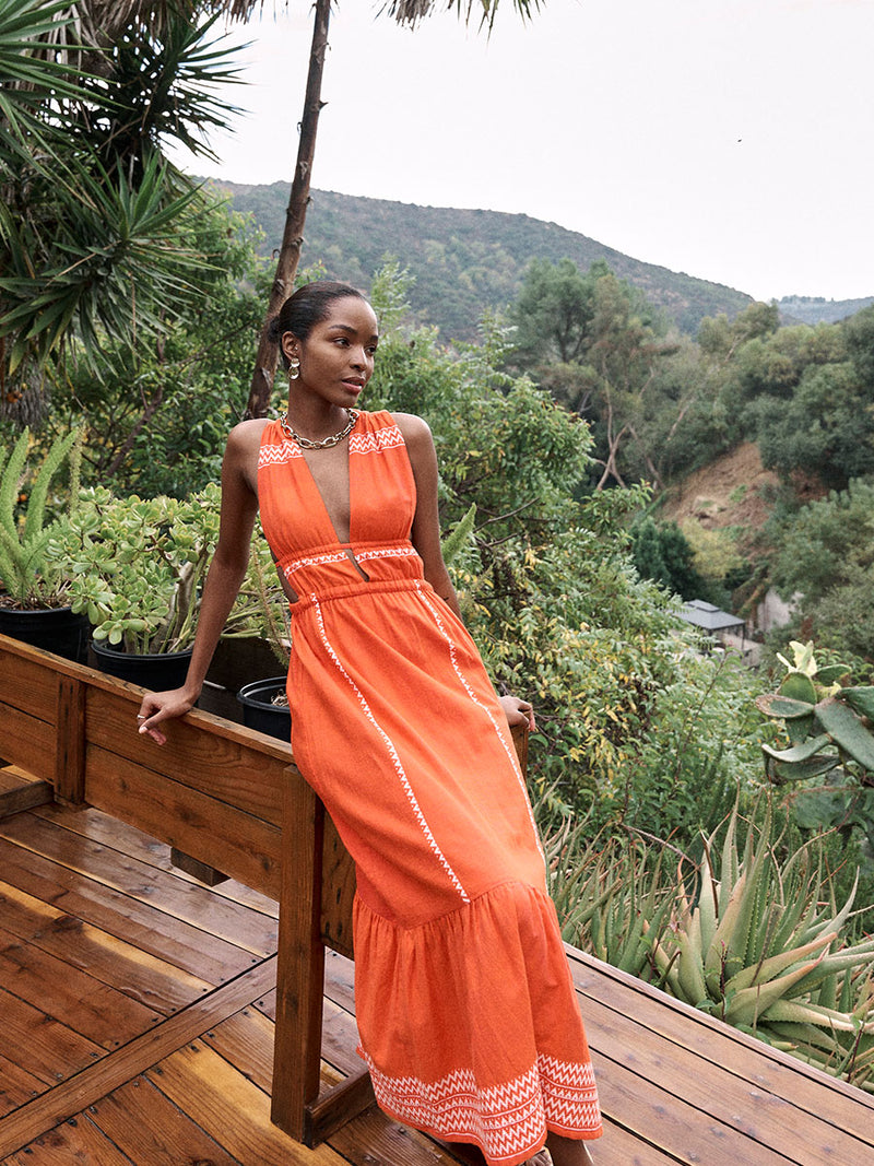 Woman sitting in the tree house Wearing lemlem LELISA Dress featuring an intricate Tibeb pattern in rich red and vanilla colors