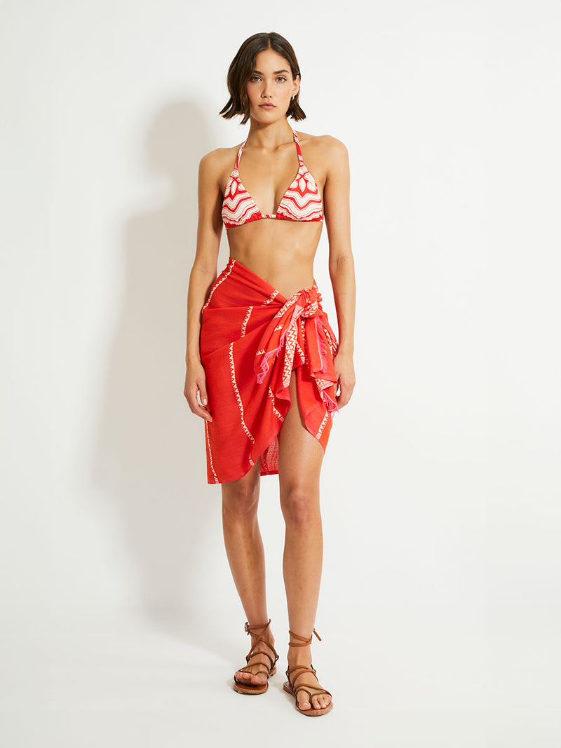 Woman Standing Wearing lemlem LEMA Sarong featuring an intricate Tibeb pattern in rich red and vanilla colors and Triangle Bikini Top 