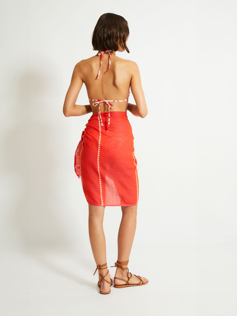 Back of a Woman Standing Wearing lemlem LEMA Sarong featuring an intricate Tibeb pattern in rich red and vanilla colors and Triangle Bikini Top 