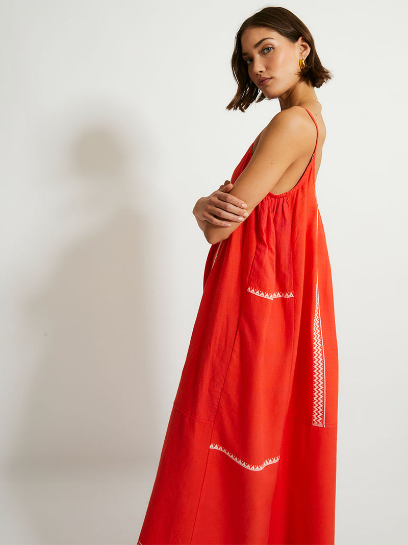 Side of a Woman Standing Wearing lemlem NIA Dress featuring an intricate Tibeb pattern in rich red and vanilla colors