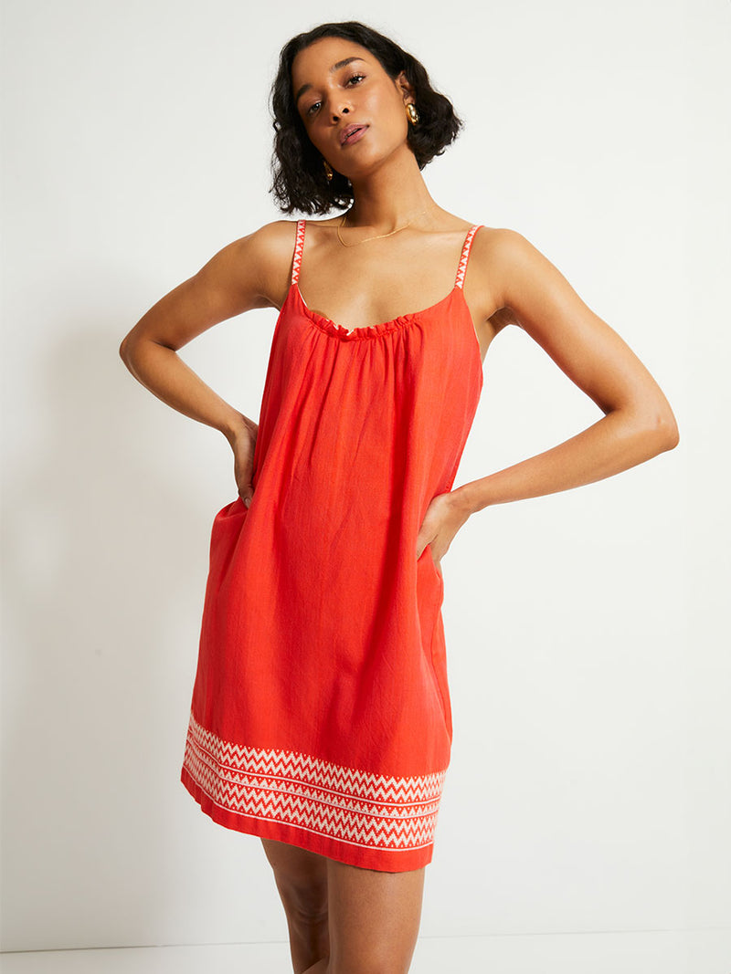 Woman Standing Wearing lemlem ZINA Dress featuring an intricate Tibeb pattern in rich red and vanilla colors