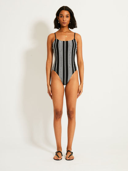 Woman standing wearing the Luchia Classic one piece swimsuit in black with white graphic diamond and arrows