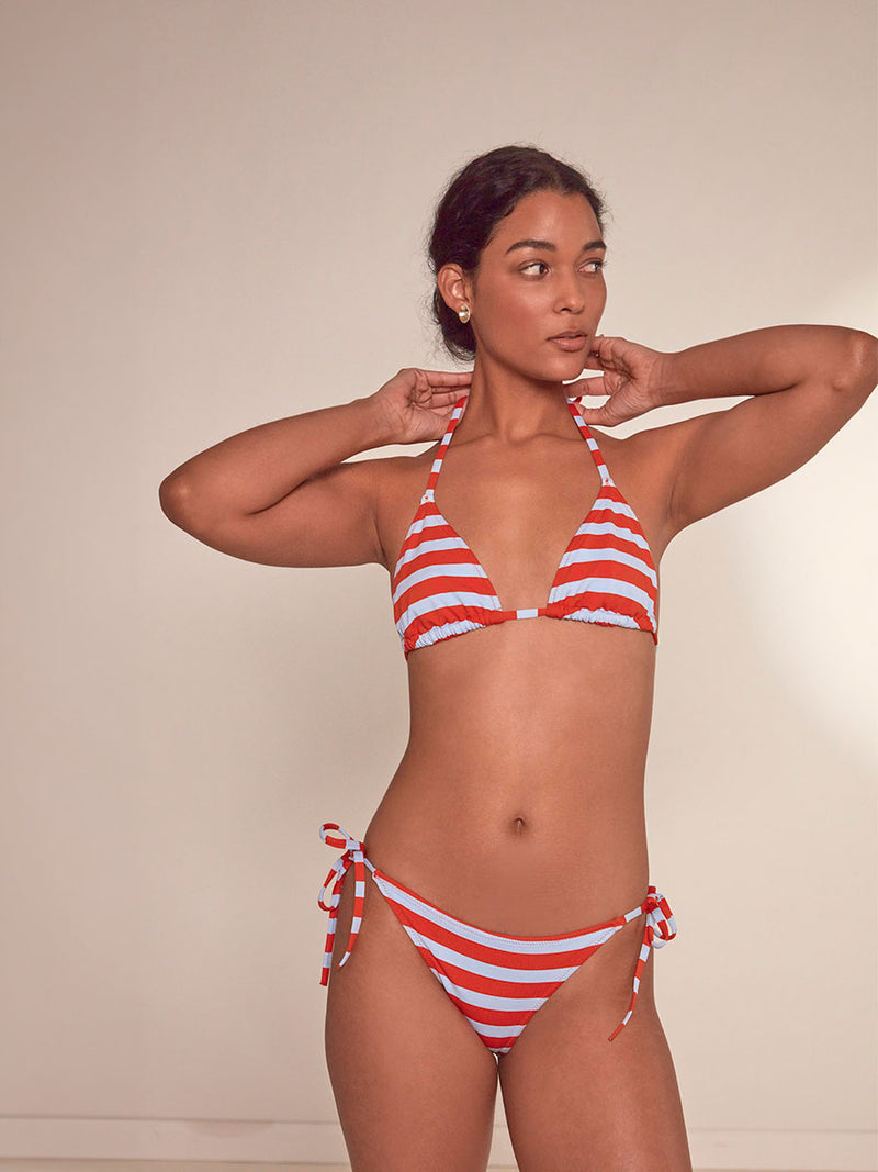 Woman Standing Wearing lemlem Malia Triangle Bikini Top featuring bold and bright tangerine color, accented by pale blue stripes and a matching bikini bottom