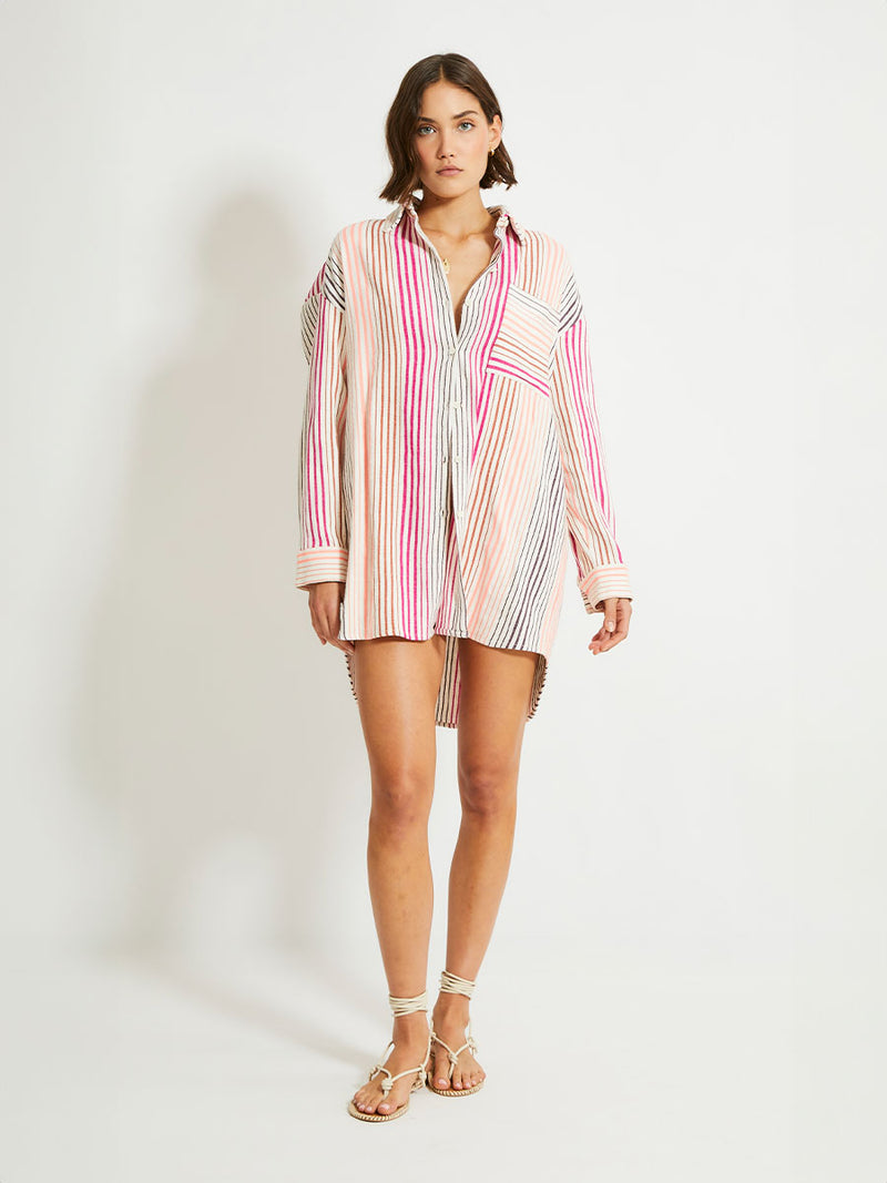 Woman Standing Wearing lemlem Mariam Shirt featuring ombre stripe pattern, where deep plum seamlessly transitions into peach, chestnut, and bright pink.