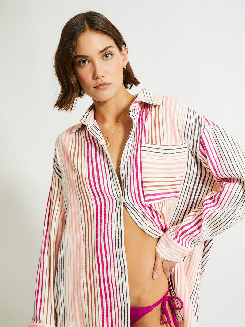 Close up on a Woman Standing Wearing lemlem Mariam Shirt featuring ombre stripe pattern, where deep plum seamlessly transitions into peach, chestnut, and bright pink.