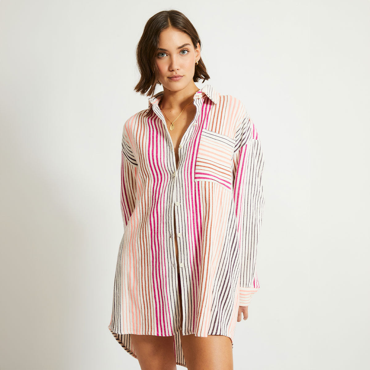 Woman standing wearing a oversized lemlem Mariam shirt in white with thin vertical pink, orange and brown stripes. 