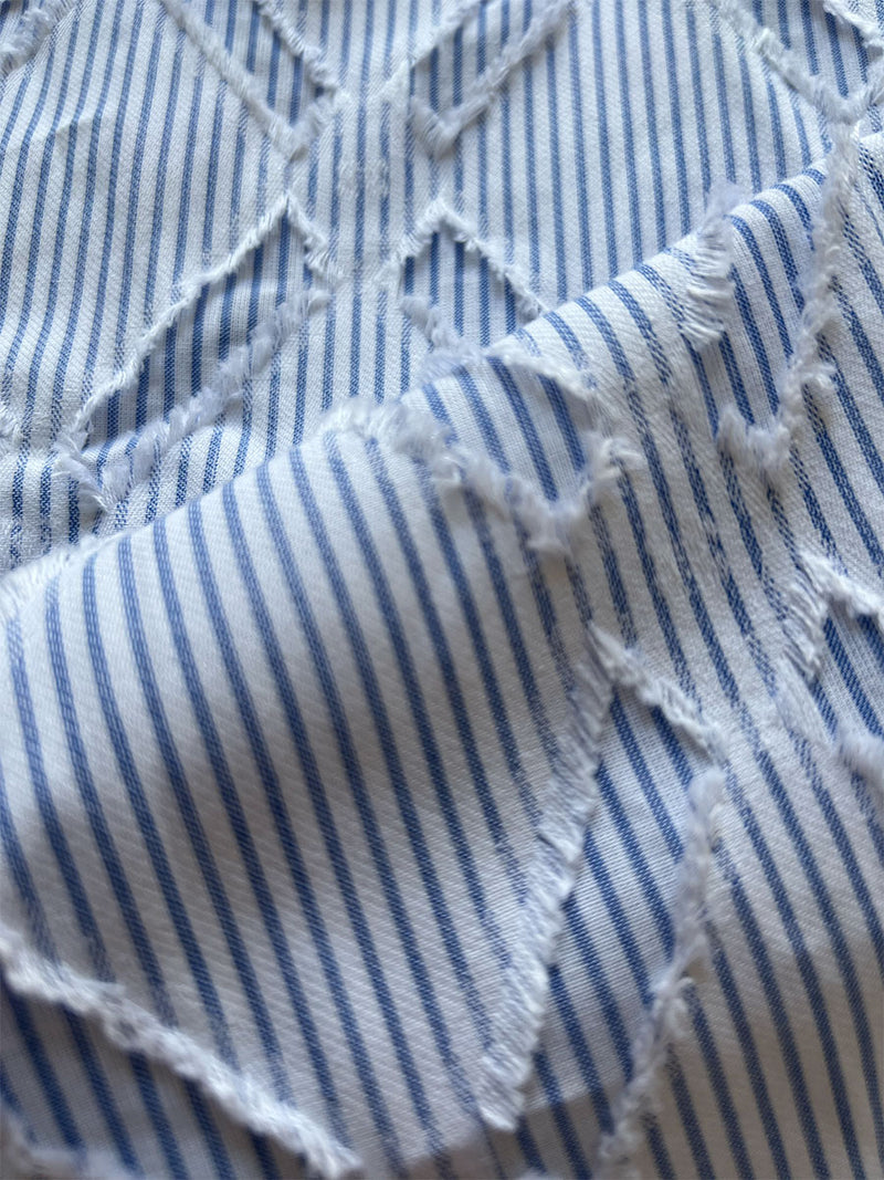close up on lemlem nefasi fabric featuring vertical stripes in a soft blue and white palette, interspersed with a delicate, crisscross pattern that adds texture.