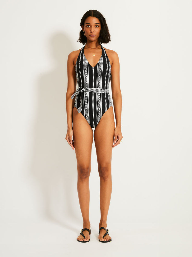 Woman standing wearing lemlem Luchia Deep V one piece swimsuit in black with graphic white diamond and arrows.