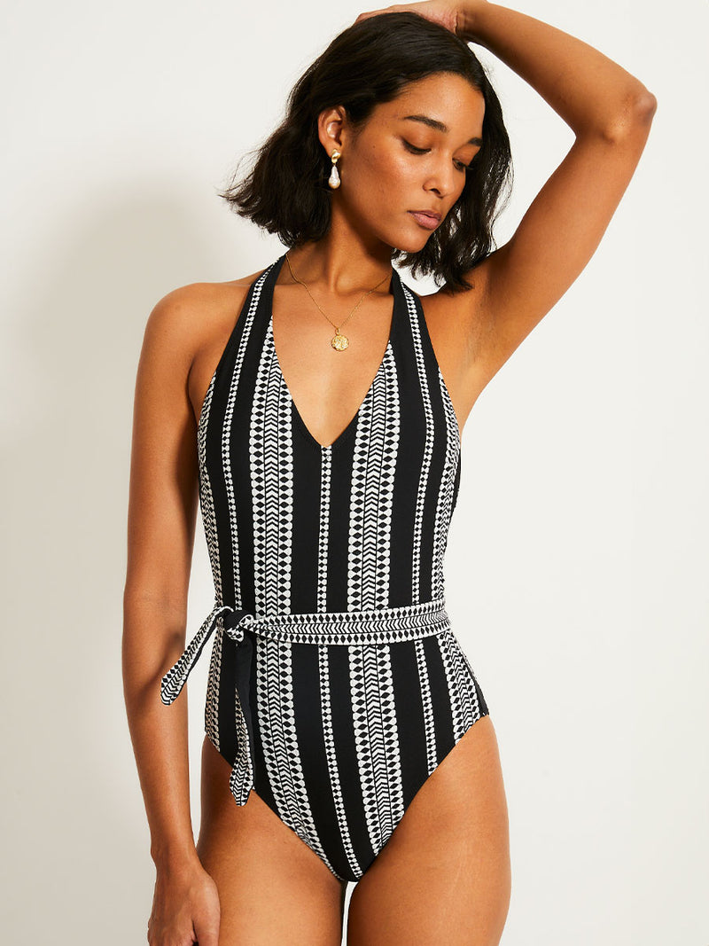 Woman standing wearing lemlem Luchia Deep V one piece swimsuit in black with graphic white diamond and arrows.