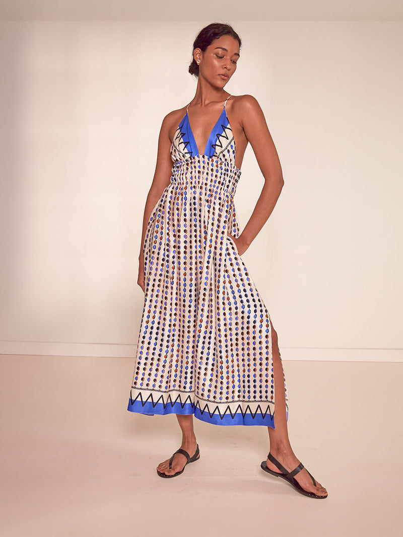 Woman Standing Wearing lemlem Gete Triangle Dress featuring diamond pattern in natural terracotta and rich blue hues against a cream background