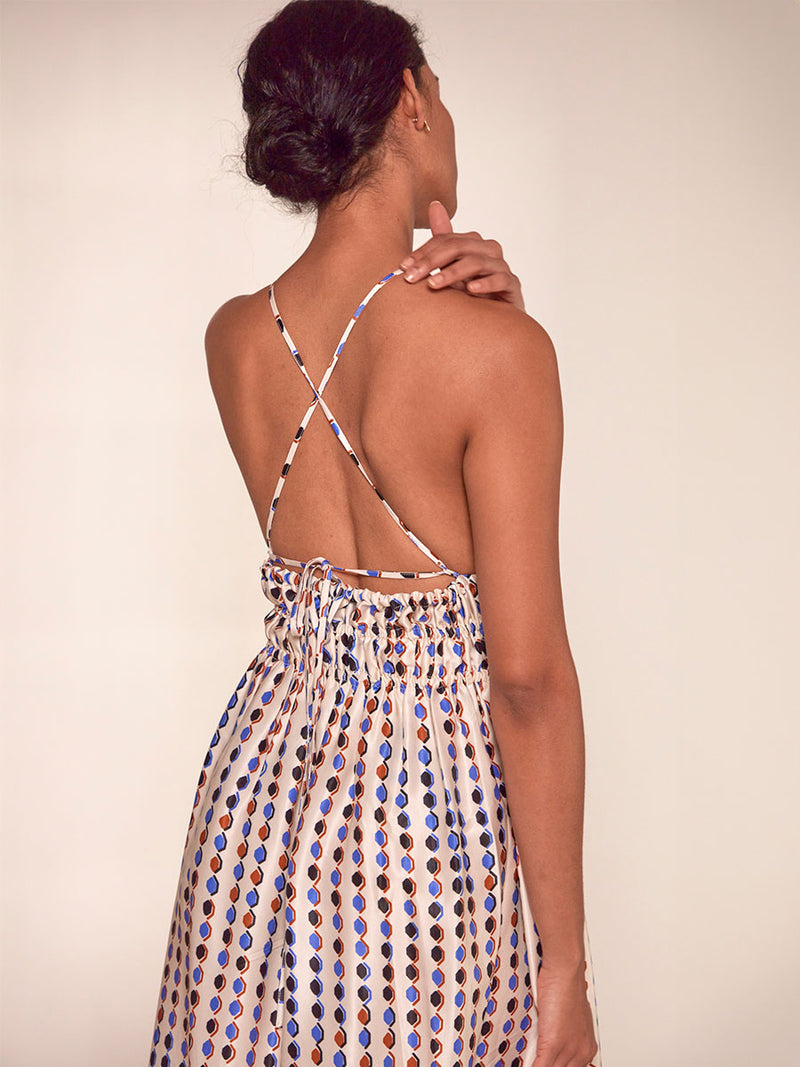 Back of a Woman Standing Wearing lemlem Gete Triangle Dress featuring diamond pattern in natural terracotta and rich blue hues against a cream background