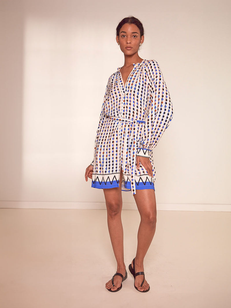 Woman Standing Wearing lemlem Meaza Button Up Dress featuring diamond pattern in natural terracotta and rich blue hues against a cream background