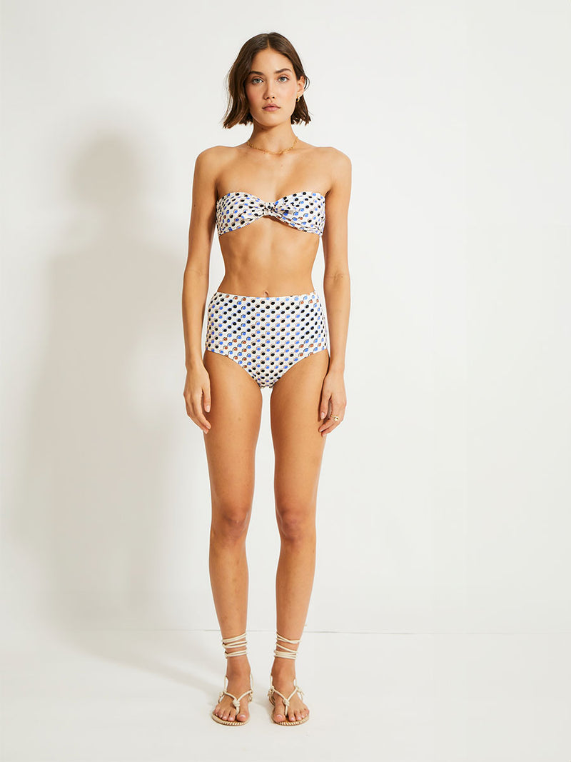 Woman Standing Wearing lemlem Elsi High Waist Bottom featuring diamond pattern in natural terracotta and rich blue hues against a cream background and matching ava bandeau top