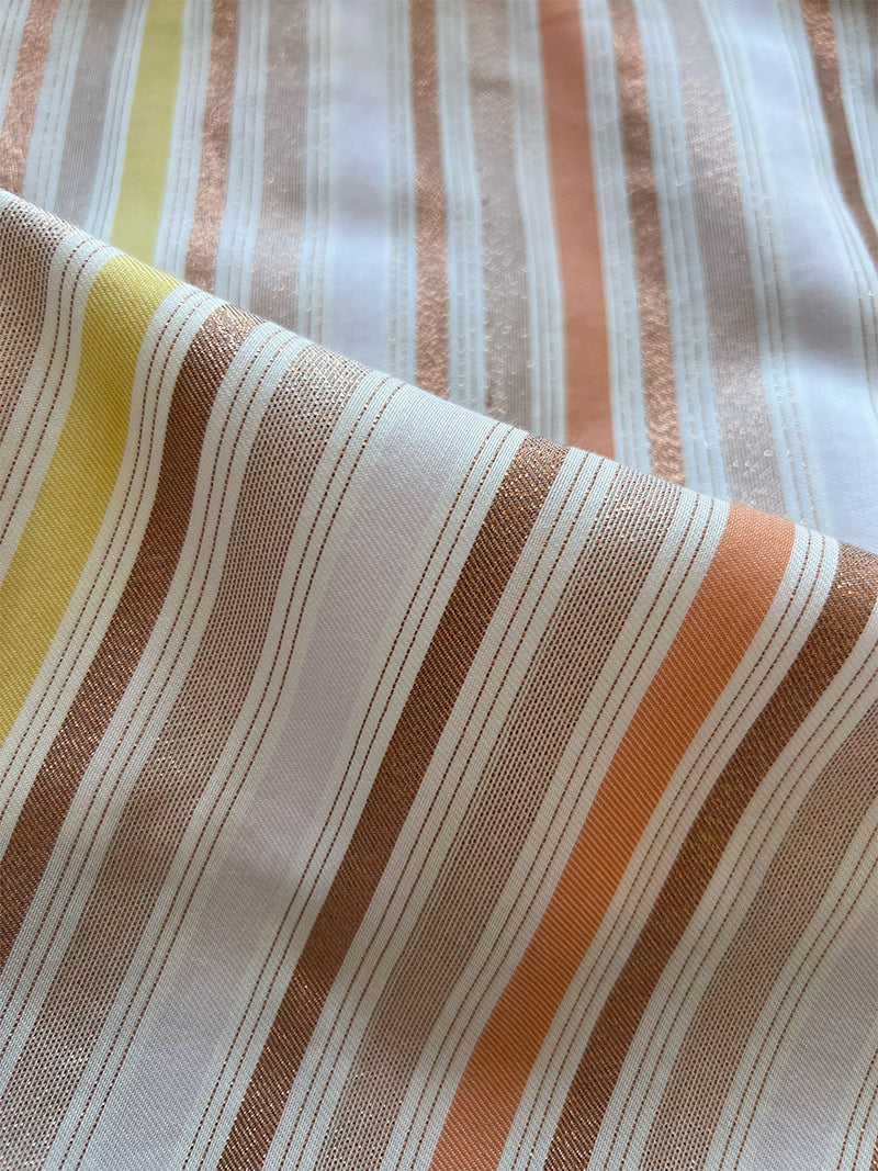 close up on lemlem retta candy fabric featuring  sunny shades of orange, pink, gold and bronze glisten in a striking stripe pattern.