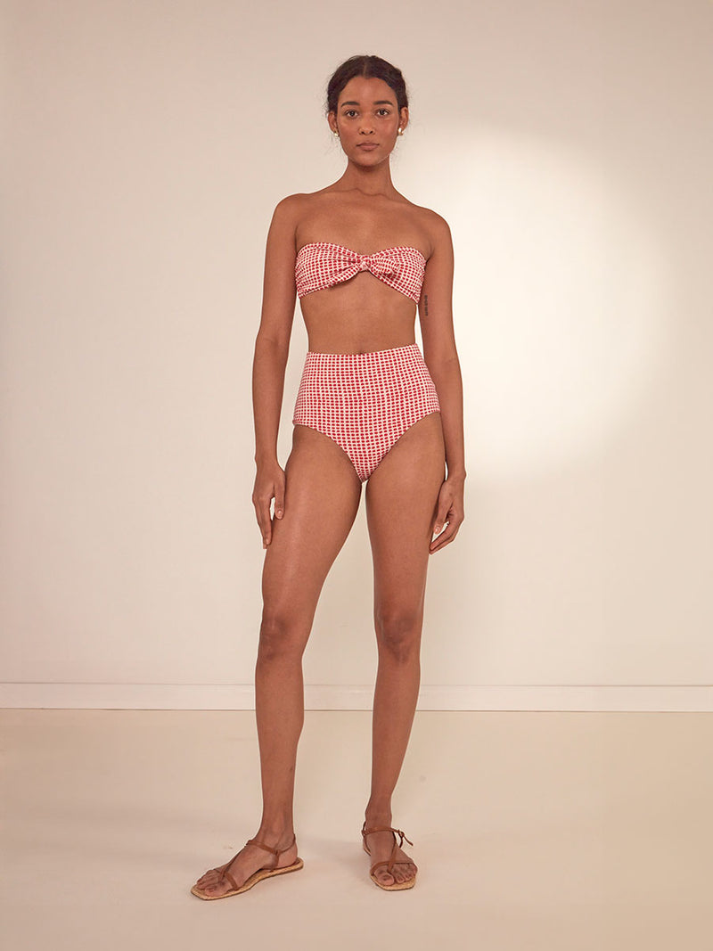 Woman Standing Wearing lemlem Ava Bandeau Top featuring vibrant raspberry dots on an ivory background and matching high waist bottom