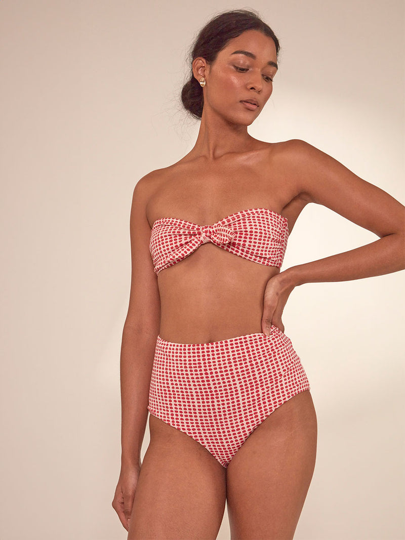 Woman Standing Wearing lemlem Elsi High Waist Bottom featuring vibrant raspberry dots on an ivory background and matching bandeau top