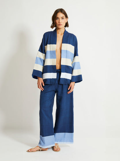 Woman Standing Wearing lemlem Desta Pants and Terrara Jacket featuring a striking color-block combination of three shades of blue, paired with bands of neutral cream and white, inspired by handmade indigo quilting and African textil.