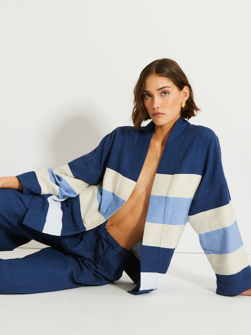 Woman sitting on the floor Wearing lemlem Desta Pants and Terrara Jacket featuring a striking color-block combination of three shades of blue, paired with bands of neutral cream and white, inspired by handmade indigo quilting and African textil.