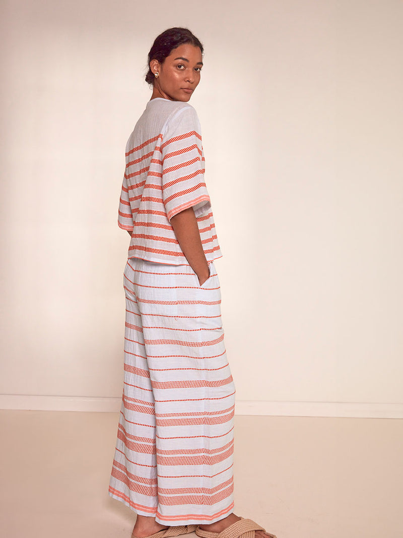 Side View of a Woman Standing Wearing lemlem Desta Pants featuring playful pattern of red dots becoming stripes on a pale blue background and matching Rita Top