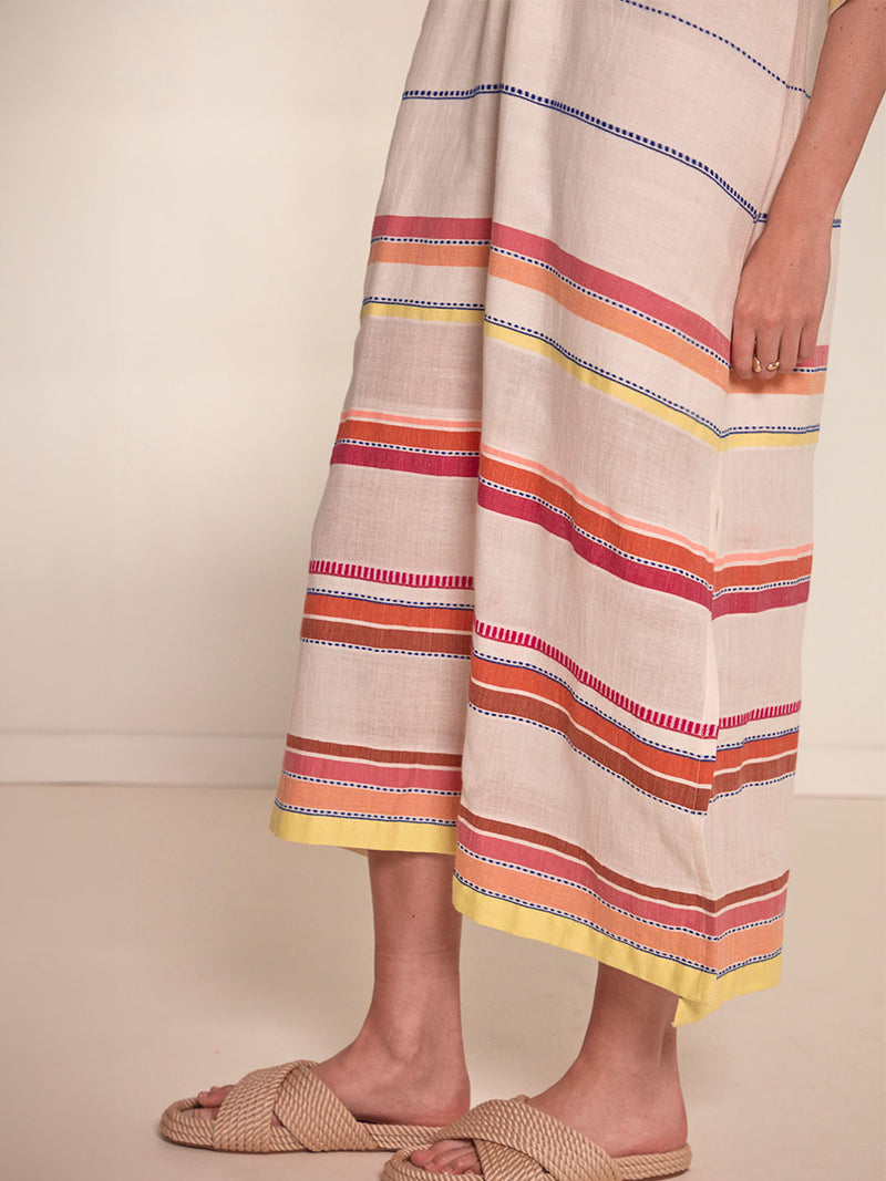 Close up on a legs of a Woman Standing Wearing lemlem Edna Dress featuring tibeb inspired stripes in a vibrant fiesta of colors against a creamy vanilla